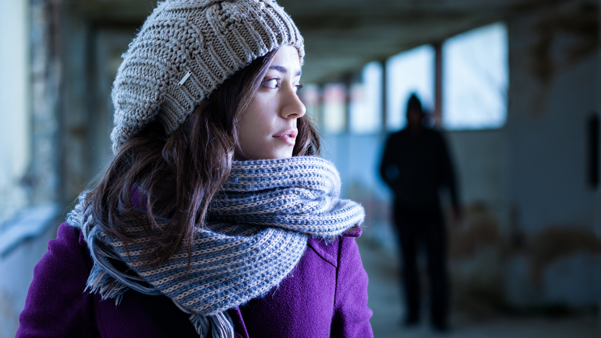 A woman looks over her shoulder in a covered walkway, with a blurred figure in the background.